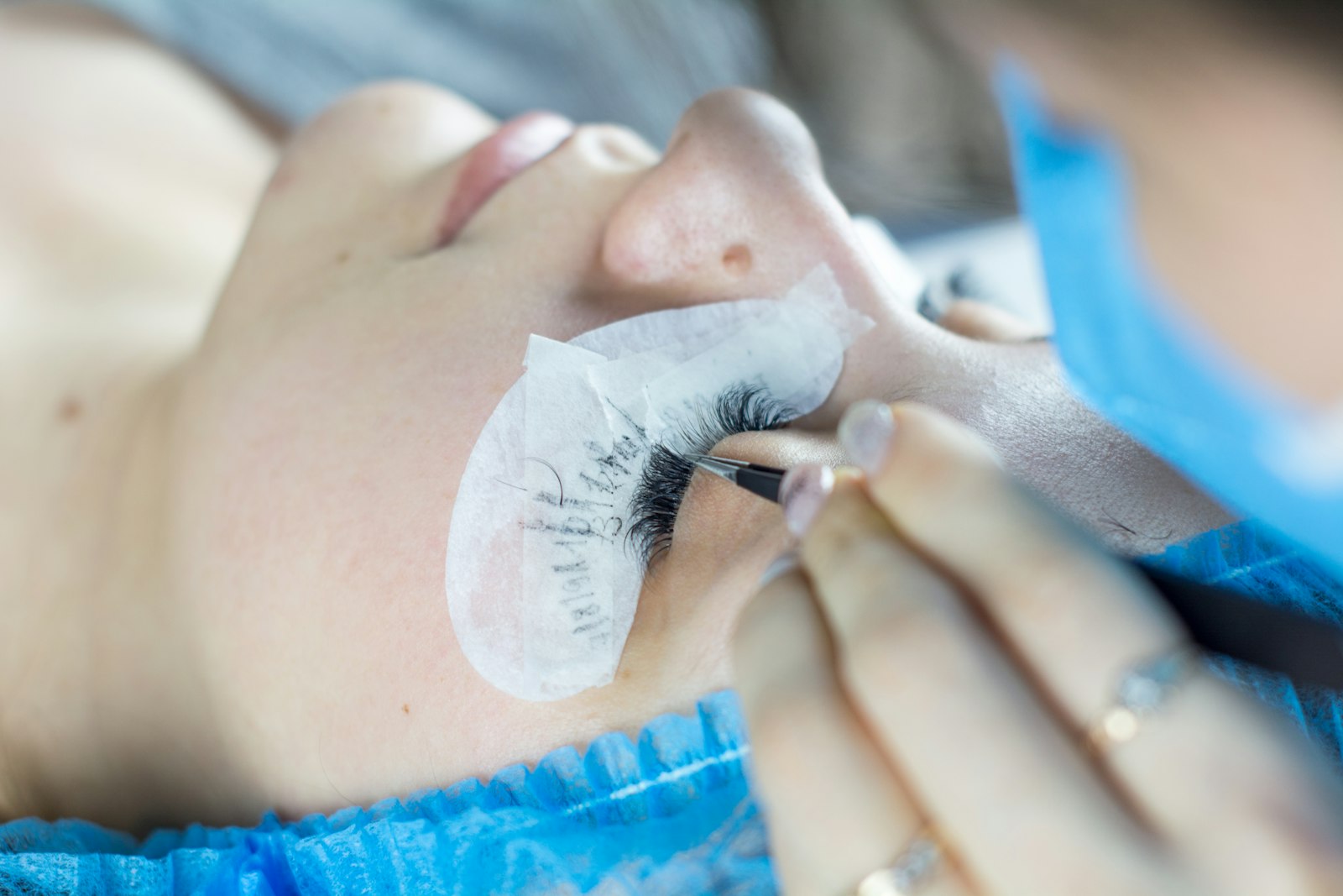 A lash technician applying eyelash extensions to a client lying on a treatment bed