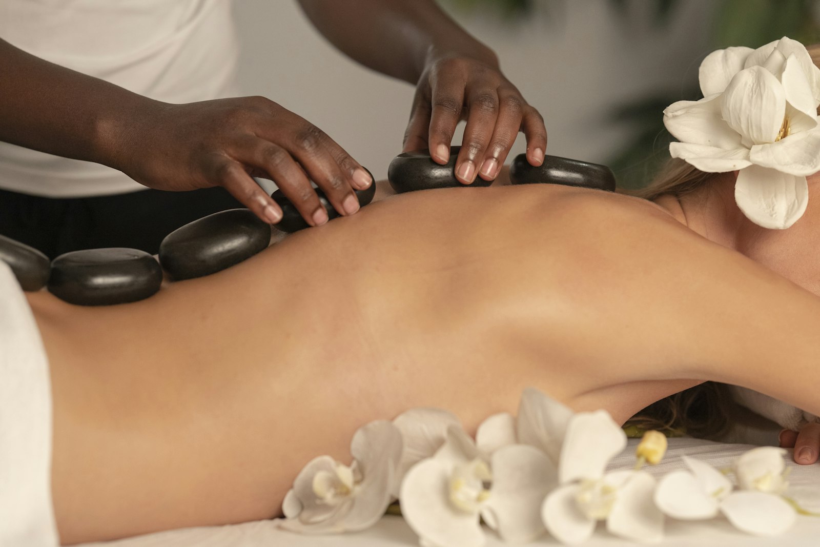 A person receiving a hot stone massage with white flowers beside the table