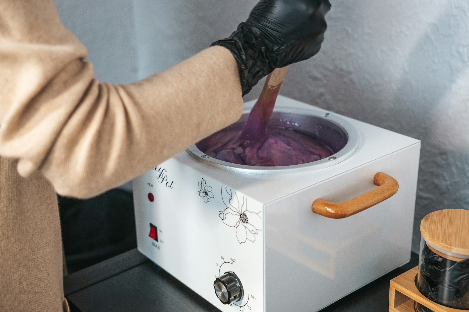 A gloved therapist stirring a pot of warm wax
